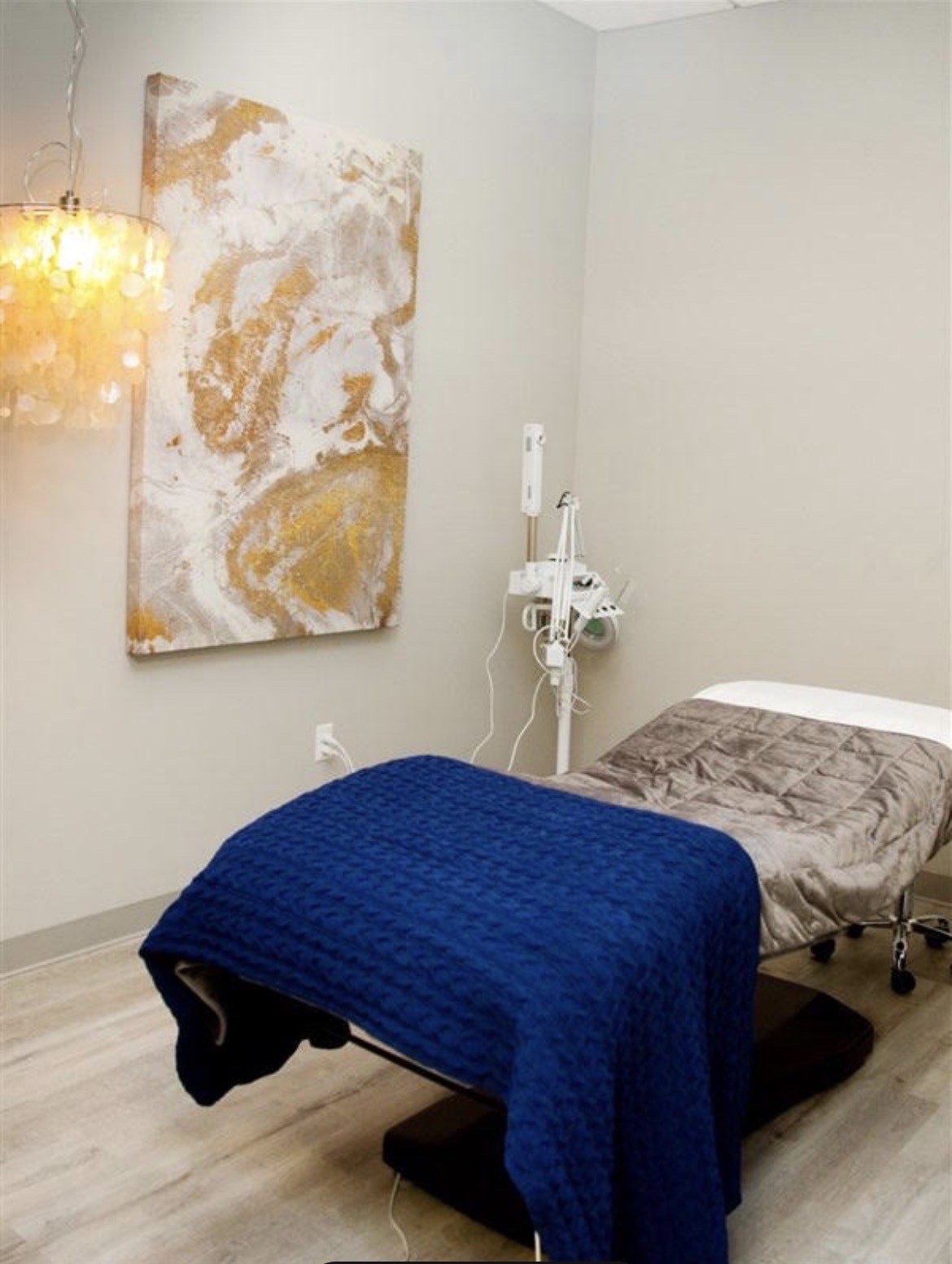 A bright treatment room with a massage table, soft blankets and a warm pendant light